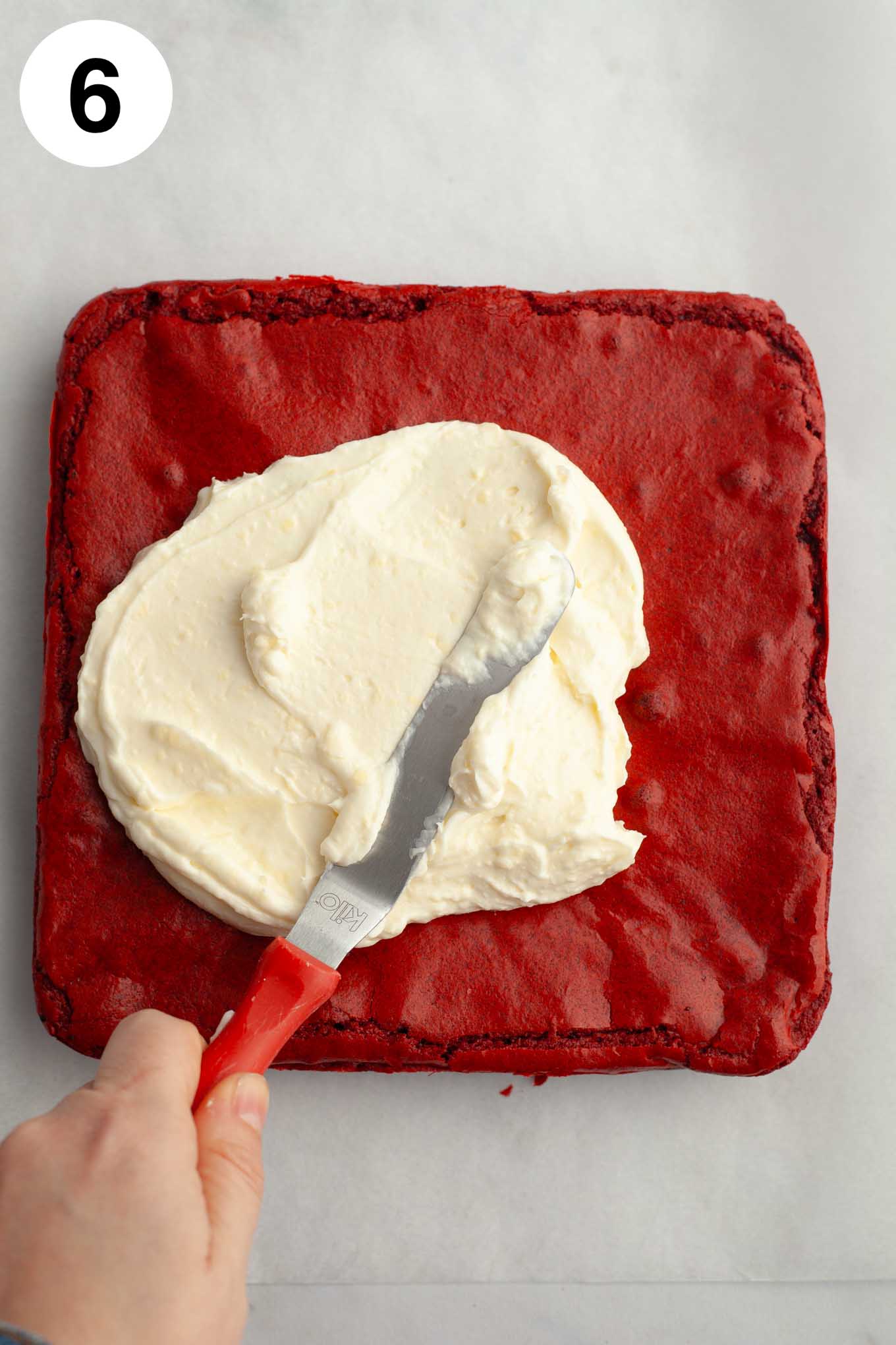 An overhead view of cream cheese icing being spread on top of the brownies with an angled spatula.