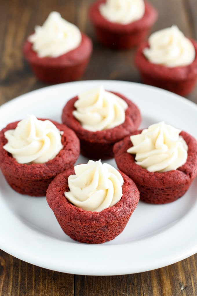 Four red velvet deep dish cookies with cream cheese frosting on a white plate. 