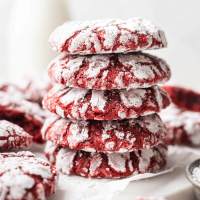 A stack of four red velvet crinkle cookies. More cookies and a small jug of milk are in the background.