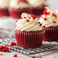 Two red velvet cupcakes topped with cream cheese frosting on a wire rack.