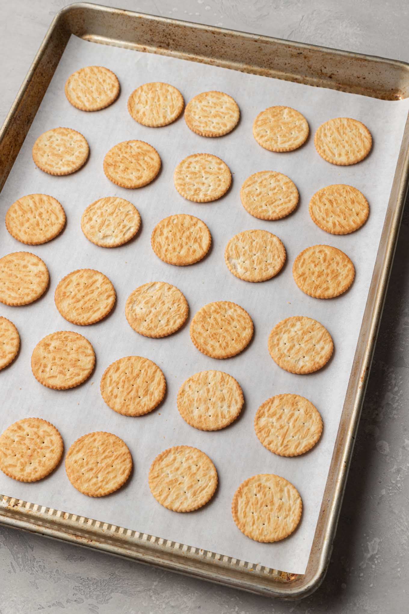 An overhead view of Ritz crackers lined up on a baking sheet. 