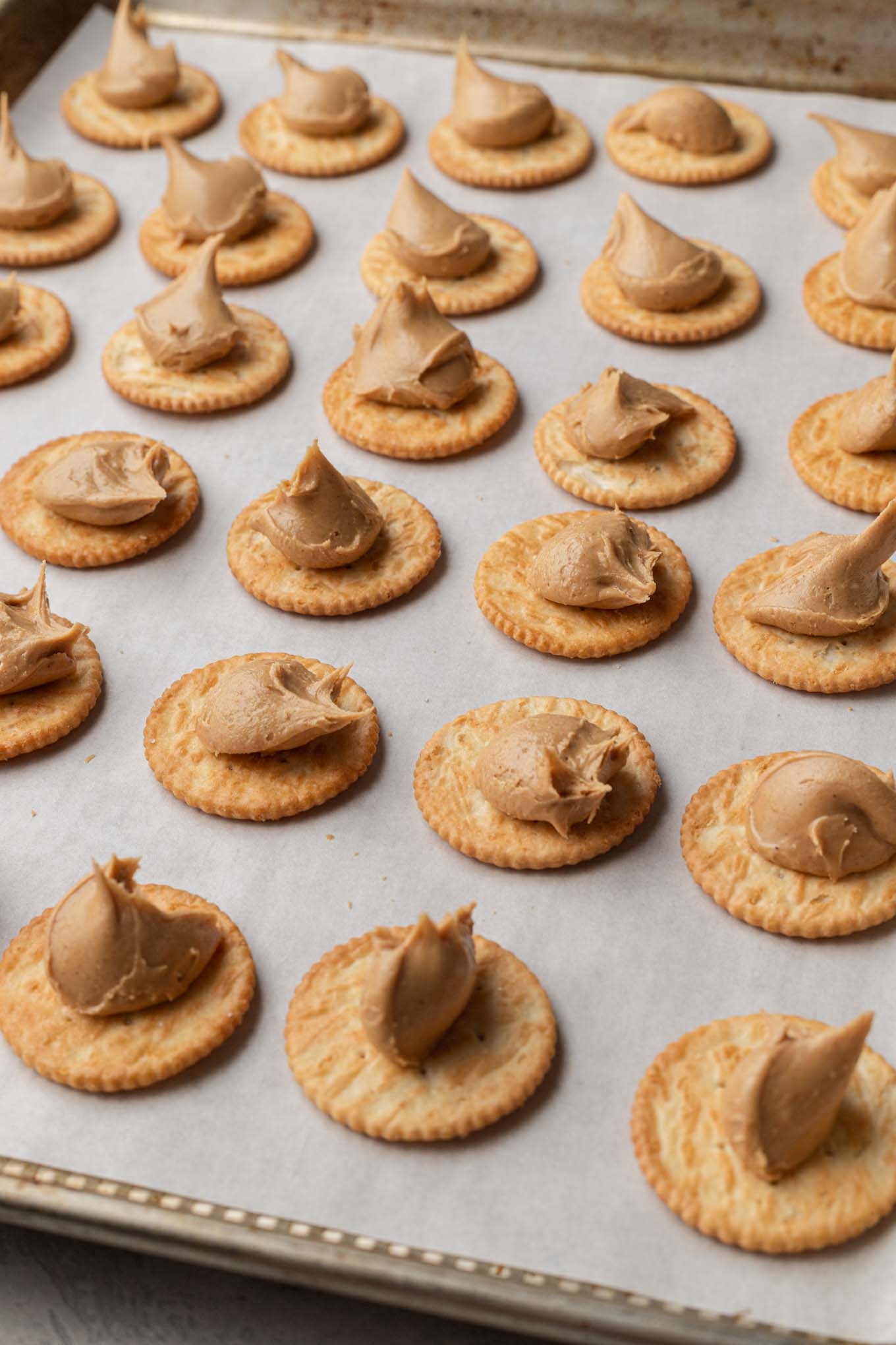 Rows of crackers dolloped with peanut butter filling, lined up on a baking sheet. 