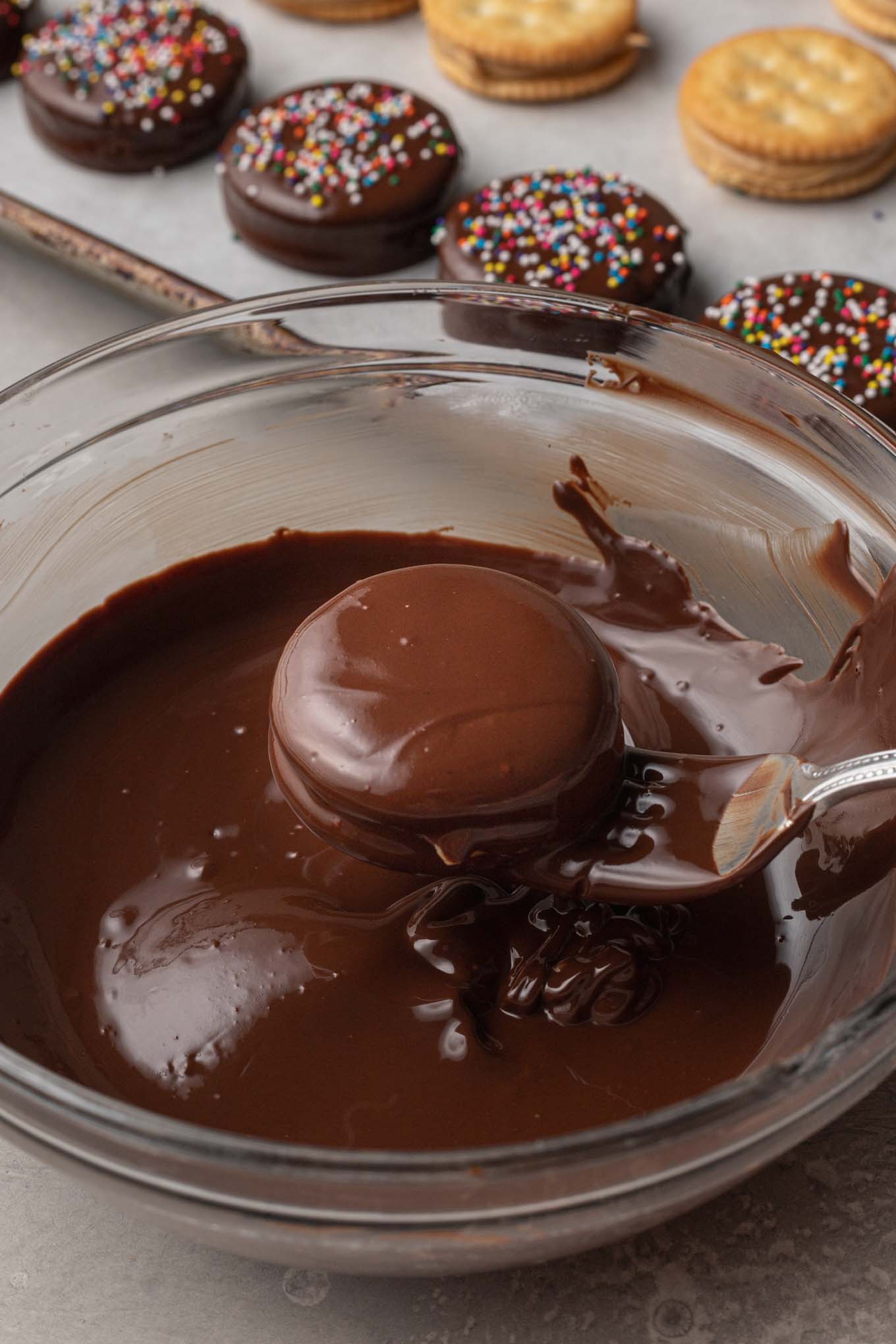 A process shot showing a Ritz cracker cookie being dipped in melted chocolate. 