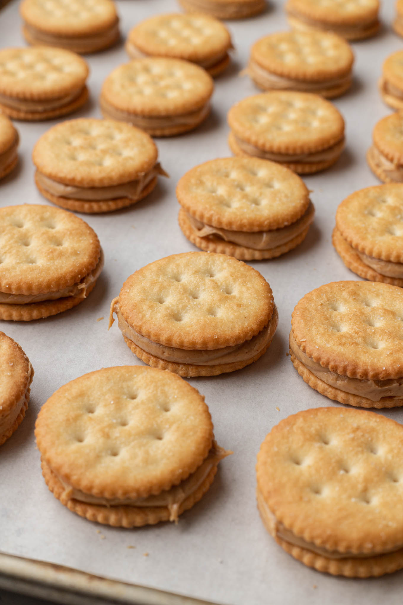 Rows of crackers filled with peanut butter, on a baking sheet. 