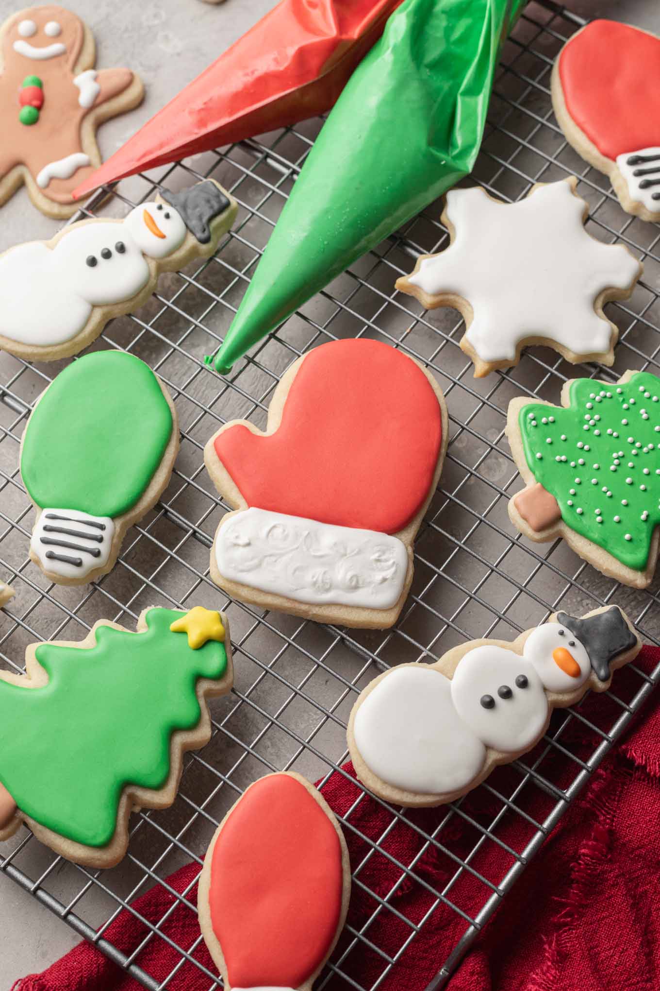 Christmas themed sugar cookies on a wire cooling rack. A bag of red and green icing are laying on the cooling rack with the cookies.