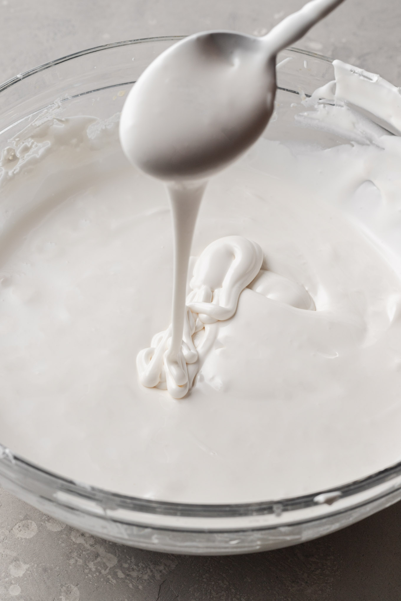 Royal icing that's been thinned to medium consistency. A spoon is lifting some of the icing out of the bowl to show the consistency.