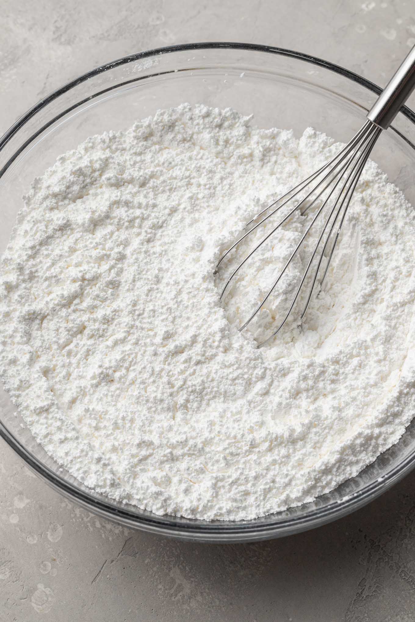 Meringue powder and powdered sugar whisked together in a glass mixing bowl.