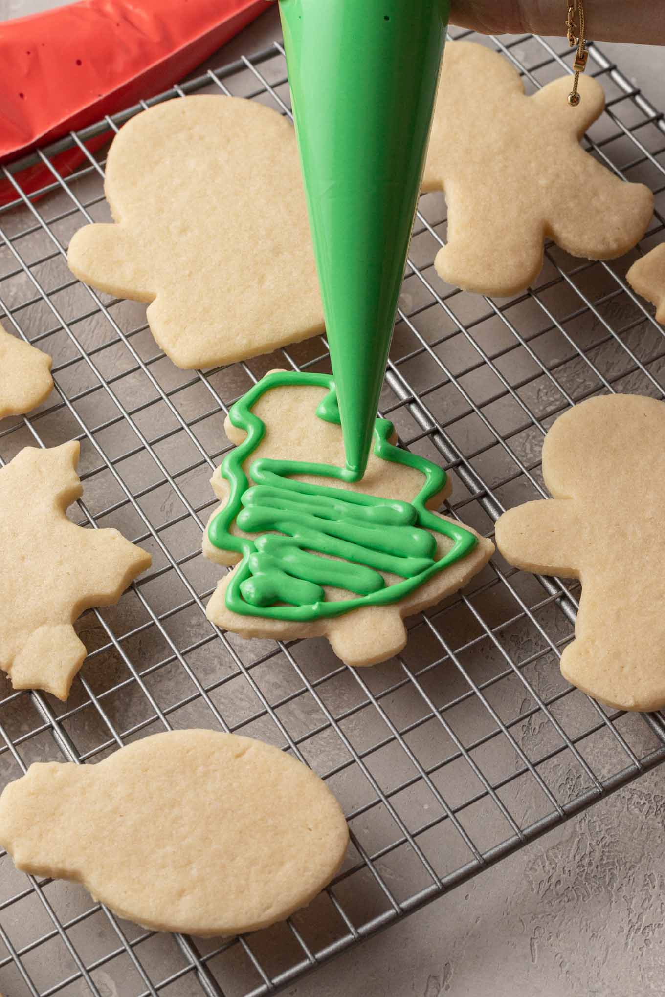 An outlined sugar cookie shaped like a tree being filled with green royal icing.