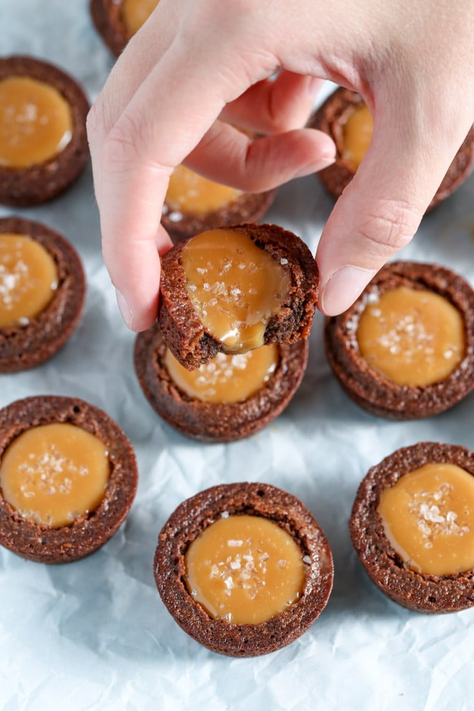 A mini brownie bite being held aloft over other brownie bites. 