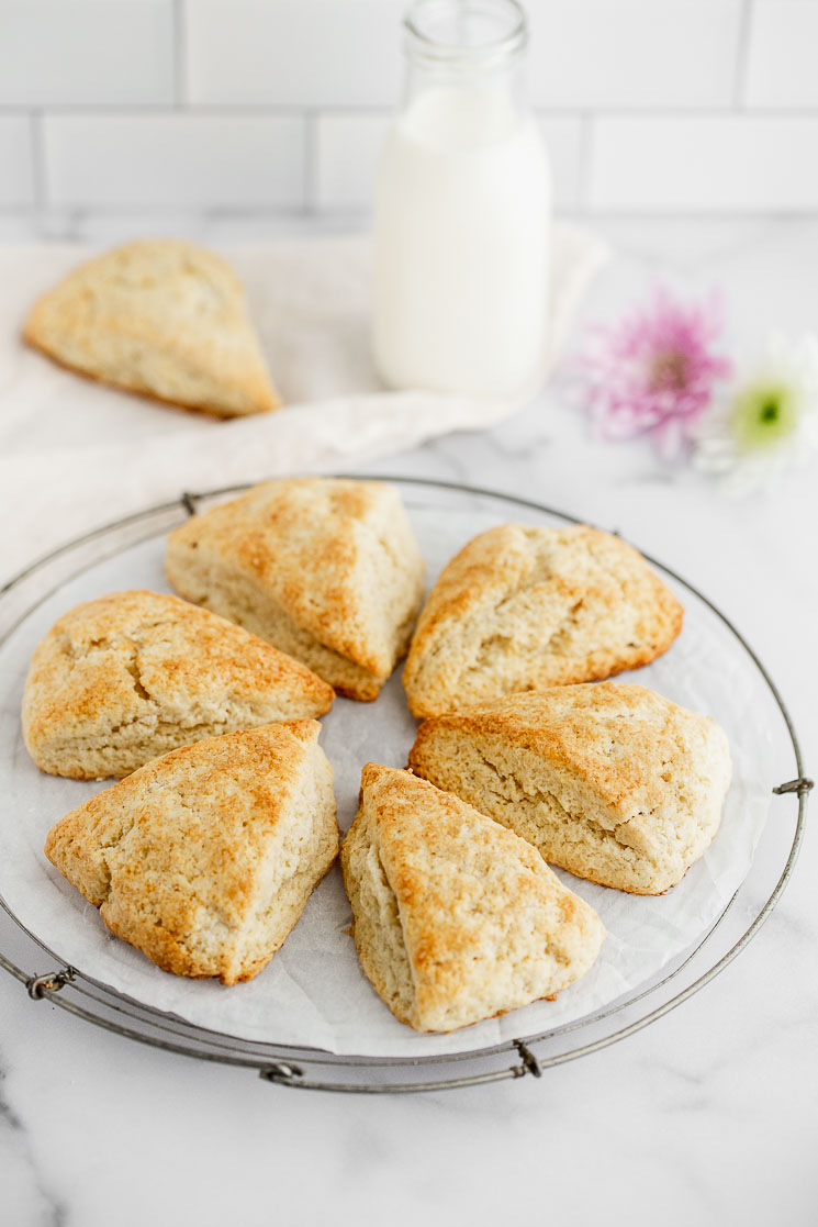 A cooling rack displaying scones in a circle with a glass of milk and flowers in the background.