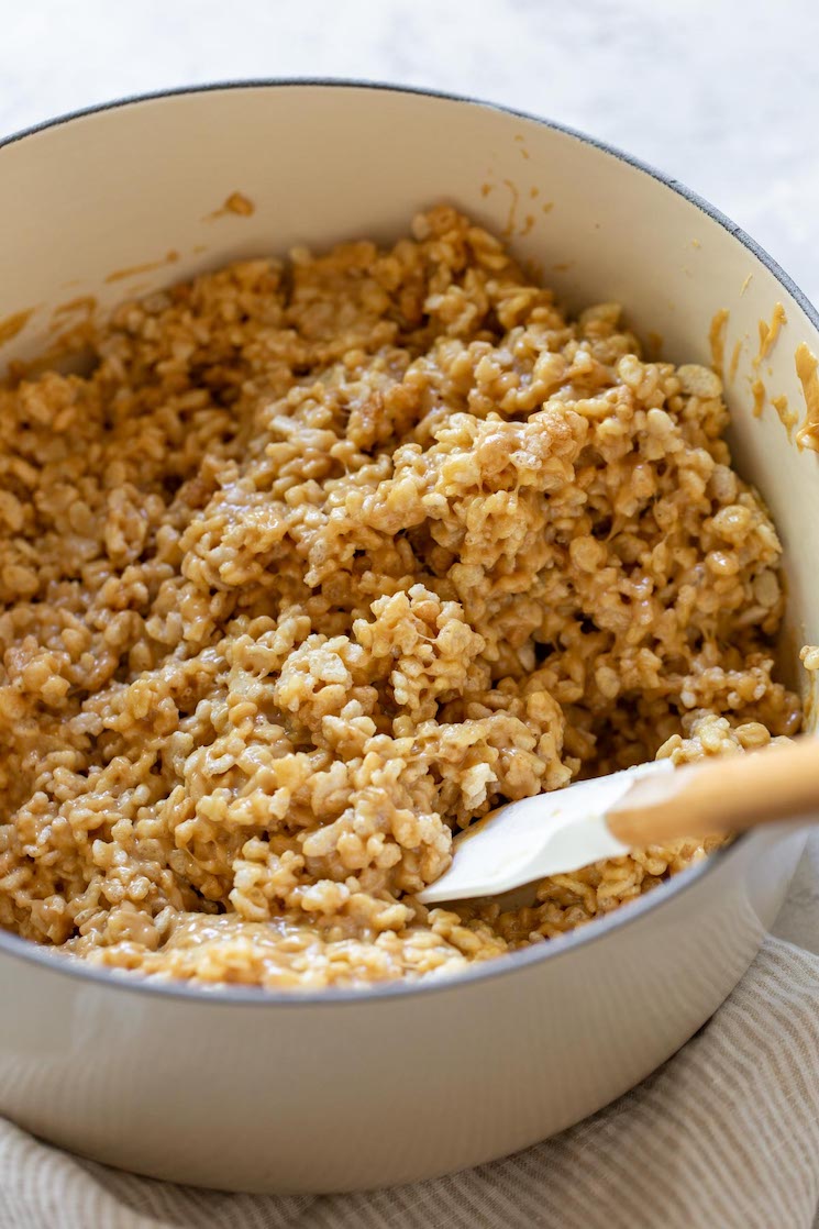 A white sauce pan with rice krispies and the melted peanut butter mixture being mixed up together. 