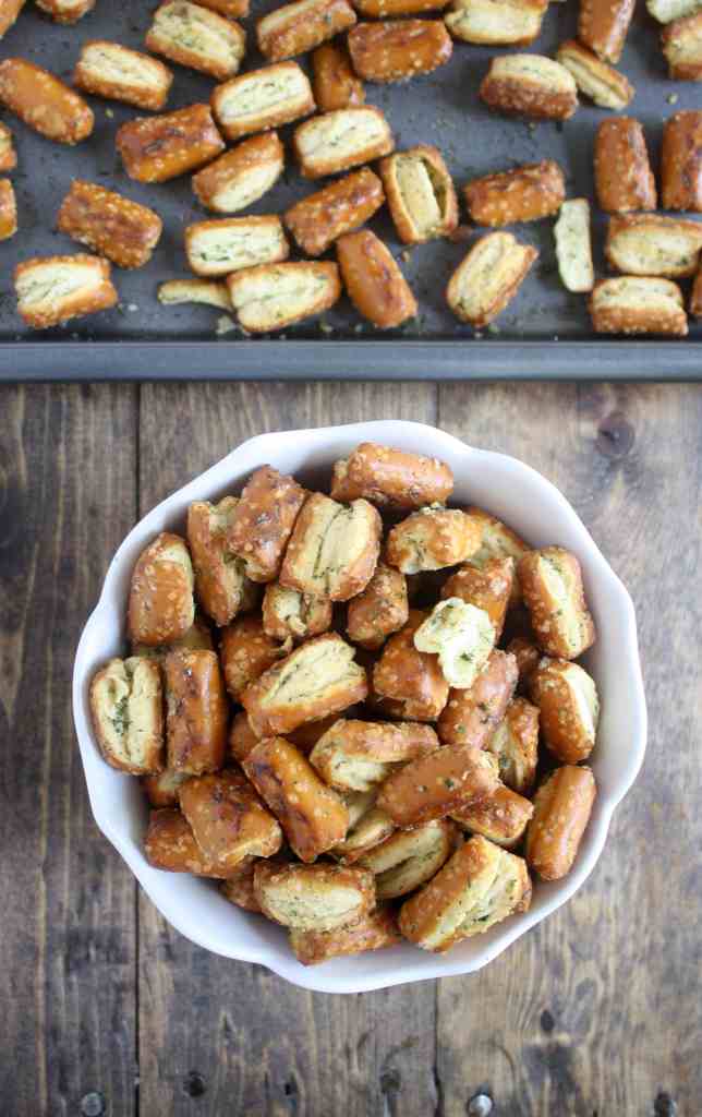 Overhead view of ranch pretzels in a white bowl next to a baking tray of pretzels. 