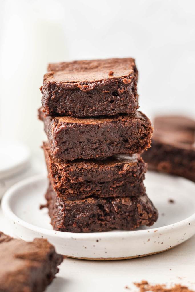 A stack of four cocoa powder brownies on a white dessert plate. 