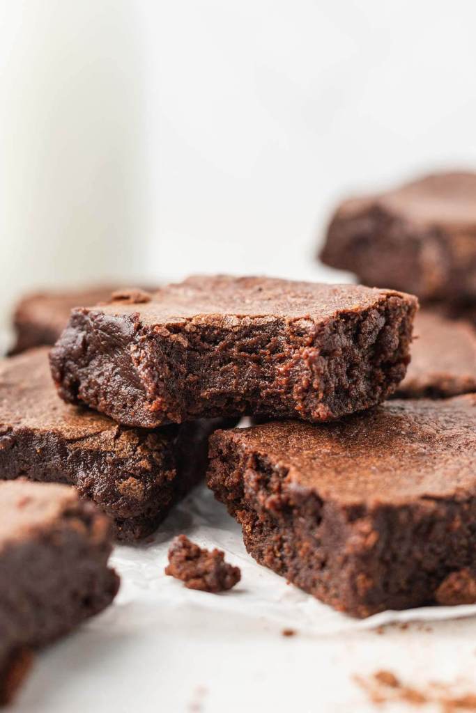 A close up view of a fudgy cocoa powder brownie with a bite missing, stacked atop additional brownies. 