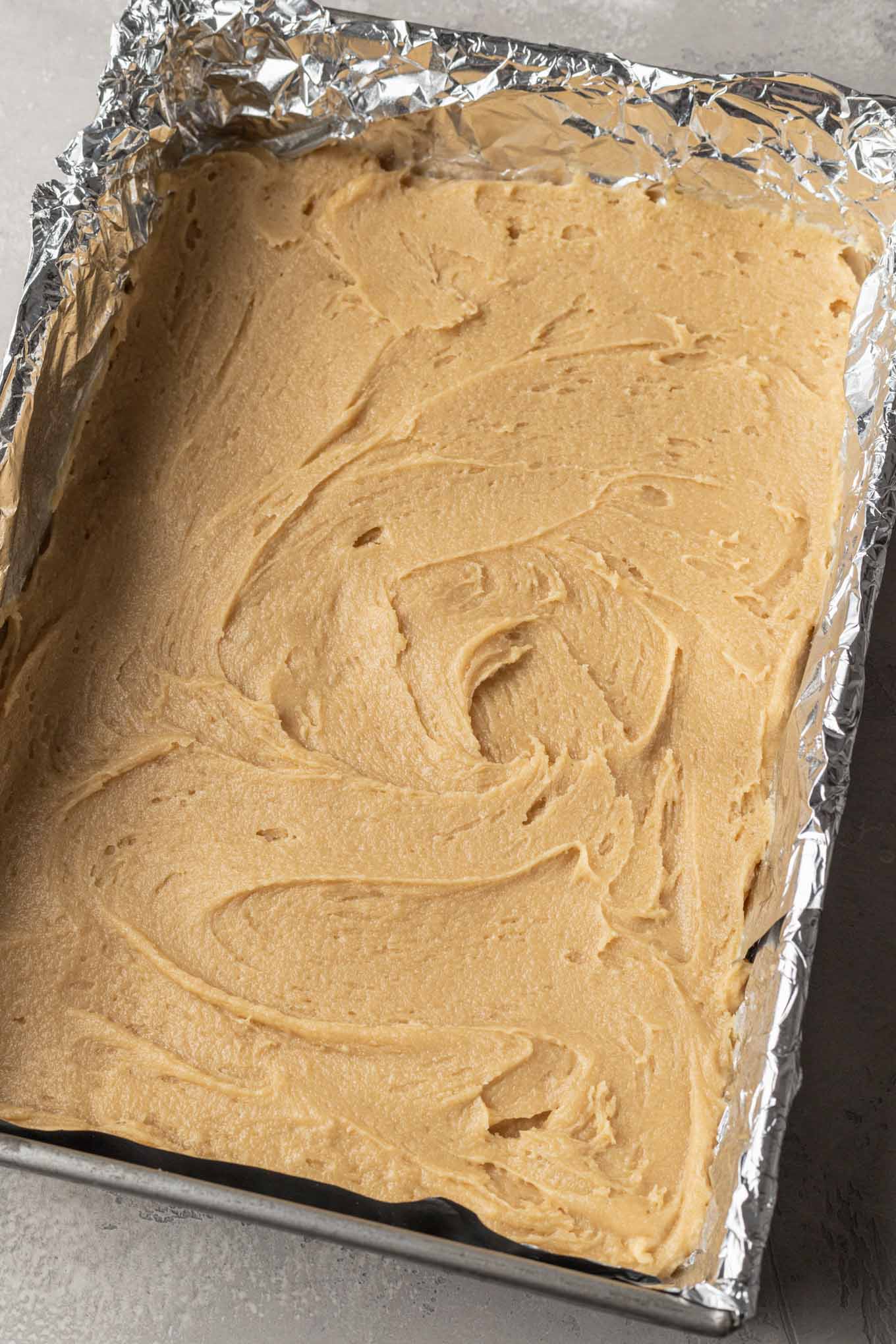 Snickerdoodle cookie dough in a 9x13 pan lined with foil.