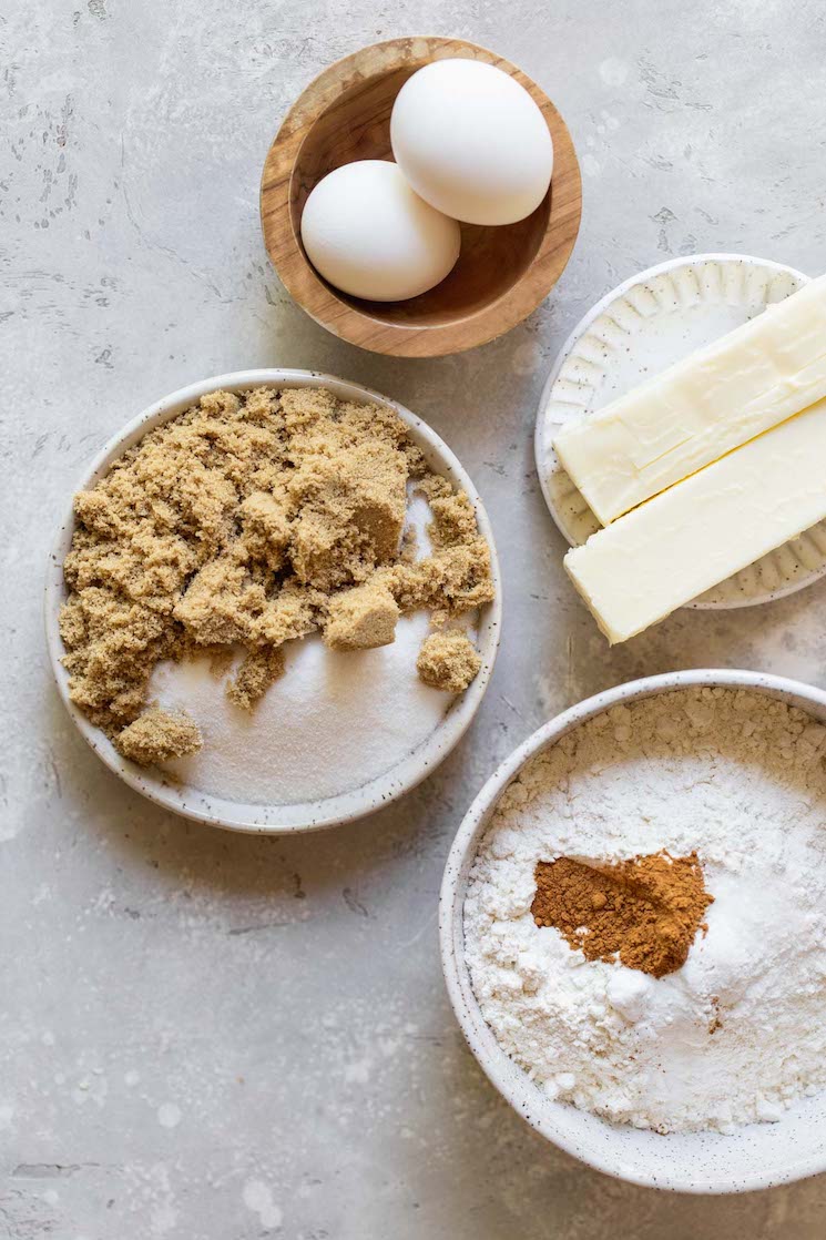 The ingredients needed to make snickerdoodle cookies on plates on a rustic gray surface.