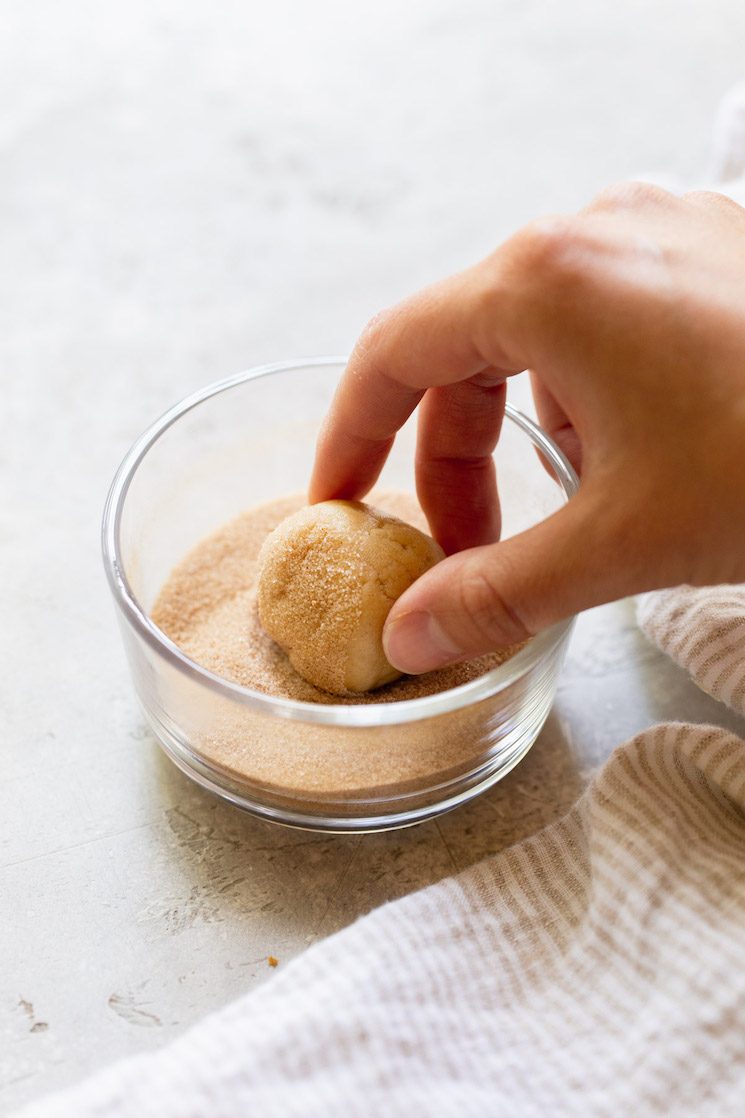 A ball of cookie dough being rolled in a cinnamon and sugar mixture.