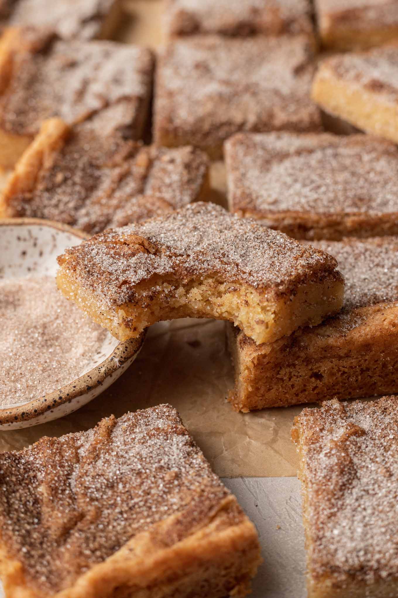 Snickerdoodle cookie bars on parchment paper. One bar has a bite missing and is resting atop the others. 