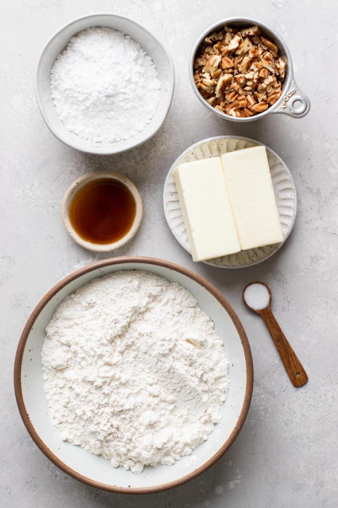 The ingredients needed to make snowball cookies laid out on a rustic gray surface.