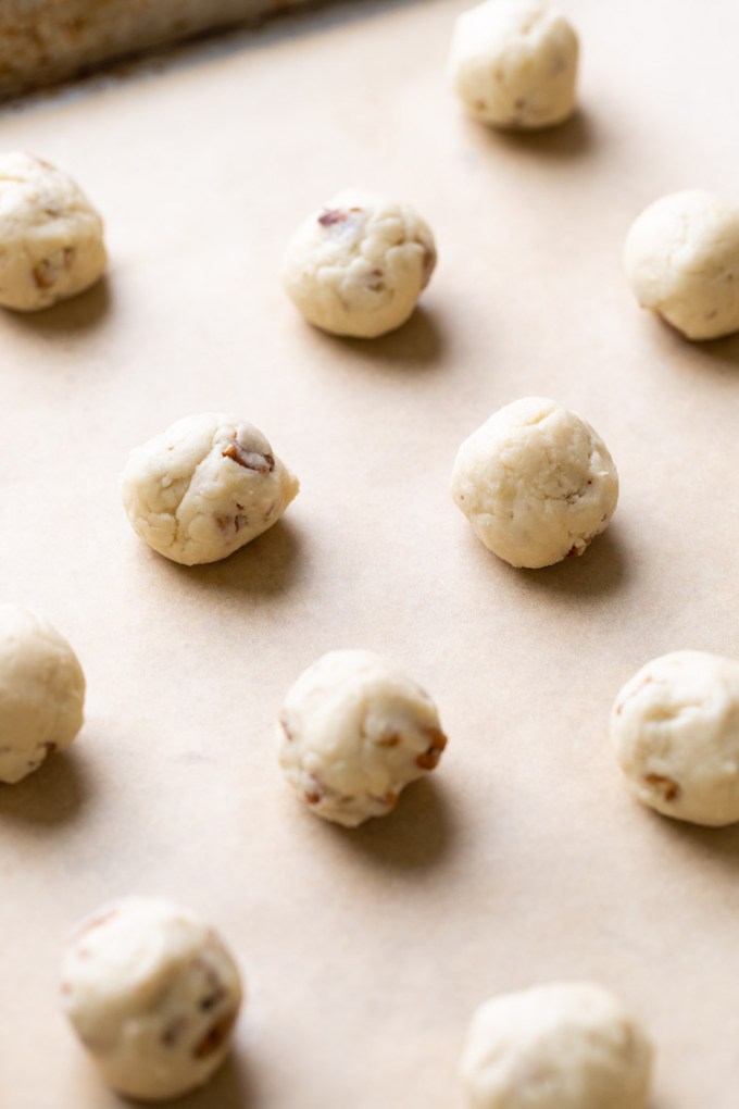 A baking sheet lined with parchment paper holding balls of cookie dough.