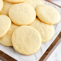 A decorative wood board covered with a stack of sugar cookies.