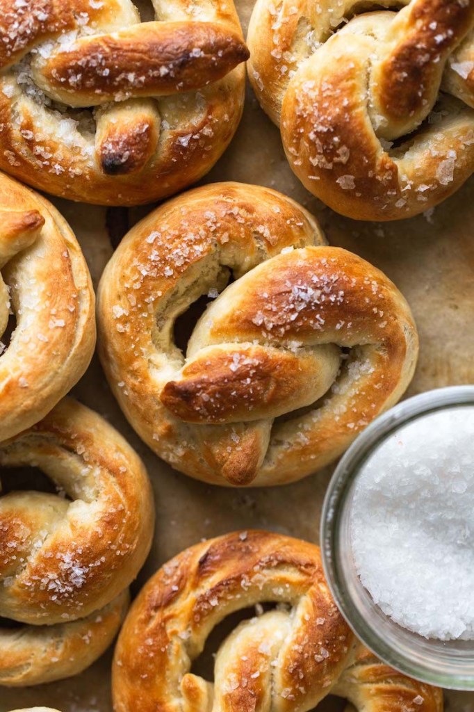 Overhead view of homemade soft pretzels on parchment paper. A dish of salt is on the side. 