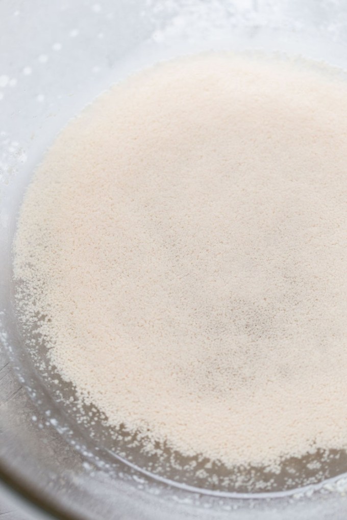 A glass mixing bowl with yeast, sugar, and water.