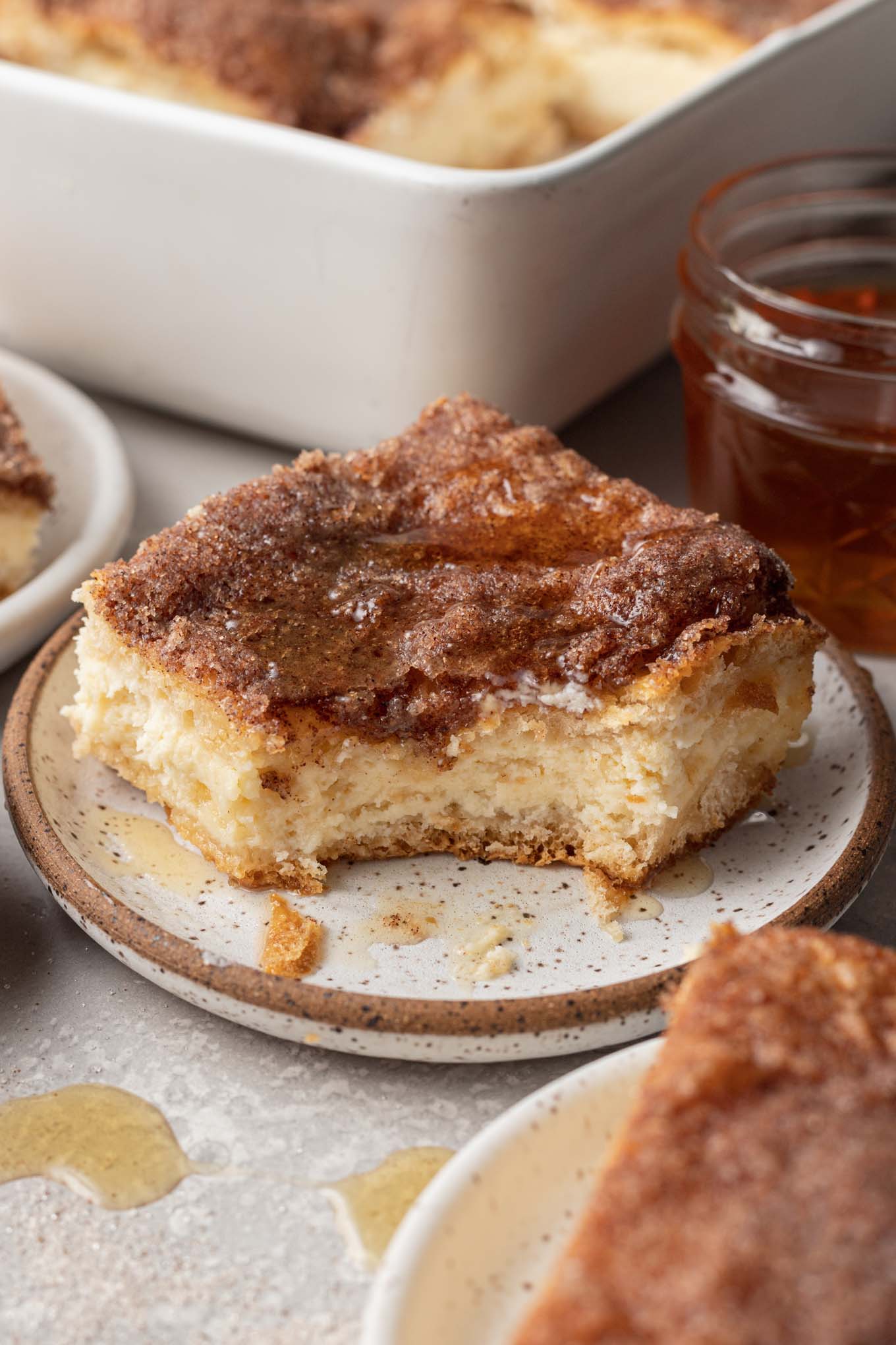 A sopapilla cheesecake bar on a speckled dessert plate, with a bite missing. 