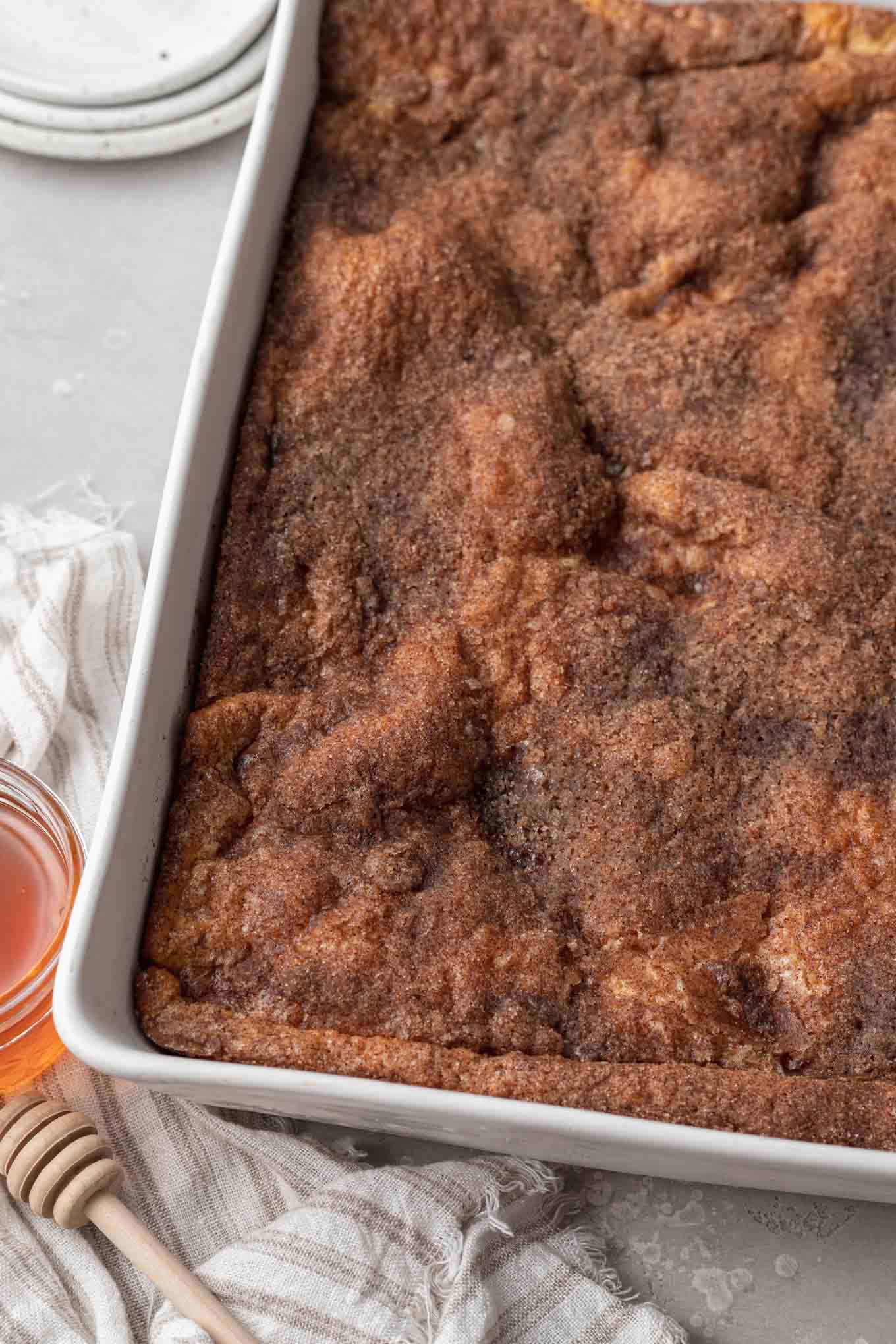 Baked sopapilla cheesecake in a large casserole dish. A jar of honey rests on the side. 