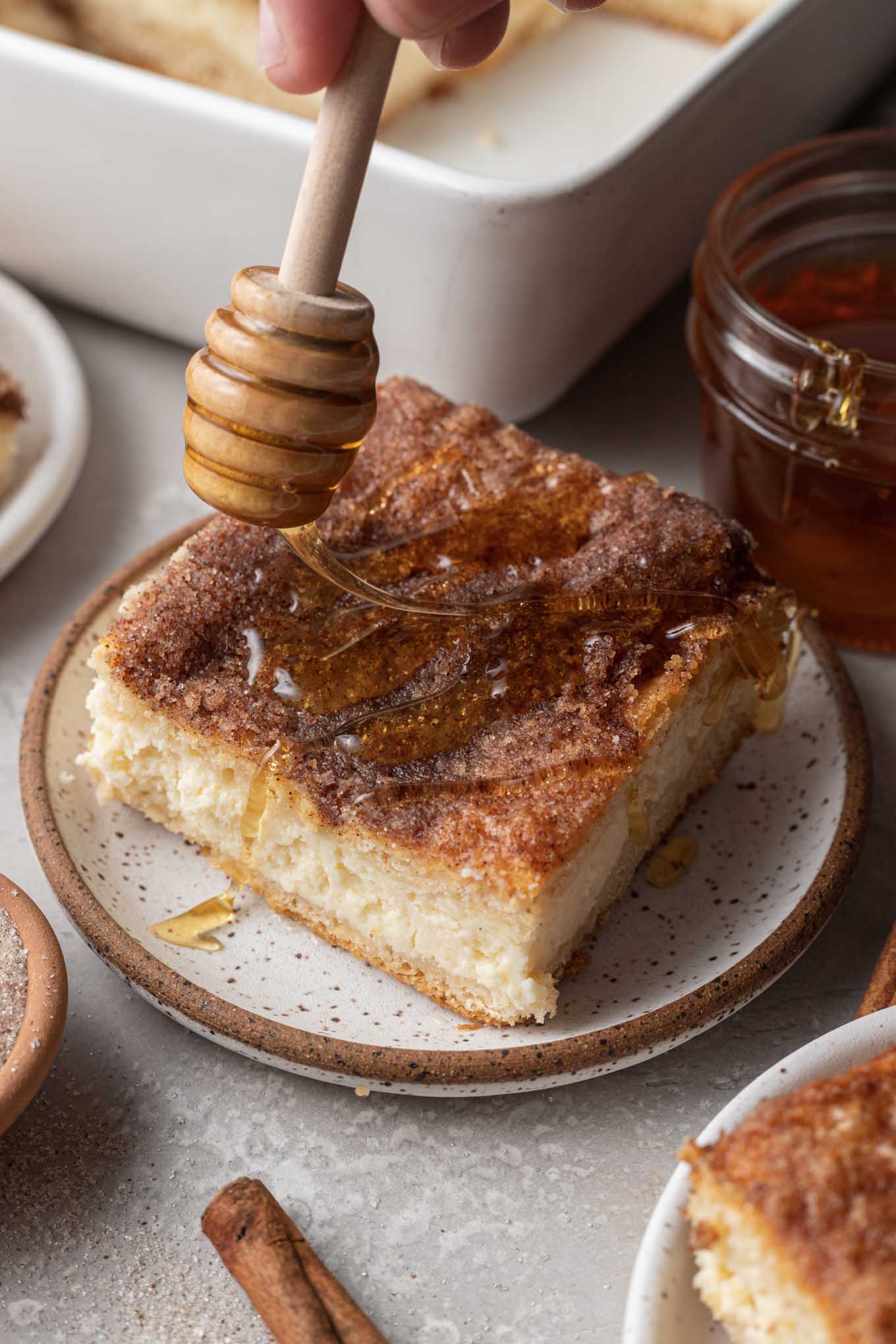 A slice of sopapilla cheesecake being drizzled with honey. 