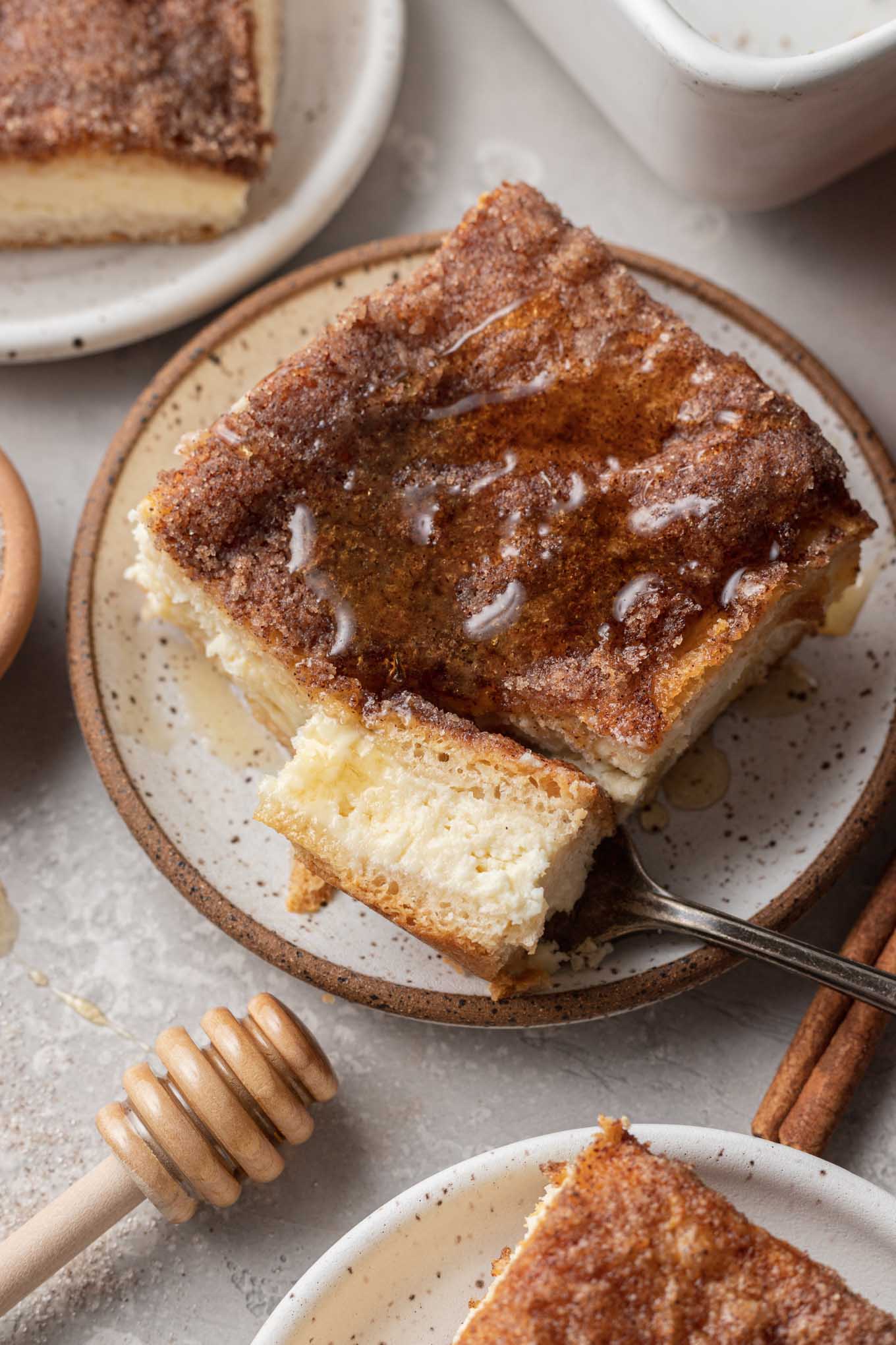 A slice of sopapilla cheesecake, drizzled with honey. A piece has been speared on a fork that rests on the plate. 