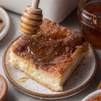 A slice of sopapilla cheesecake being drizzled with honey.