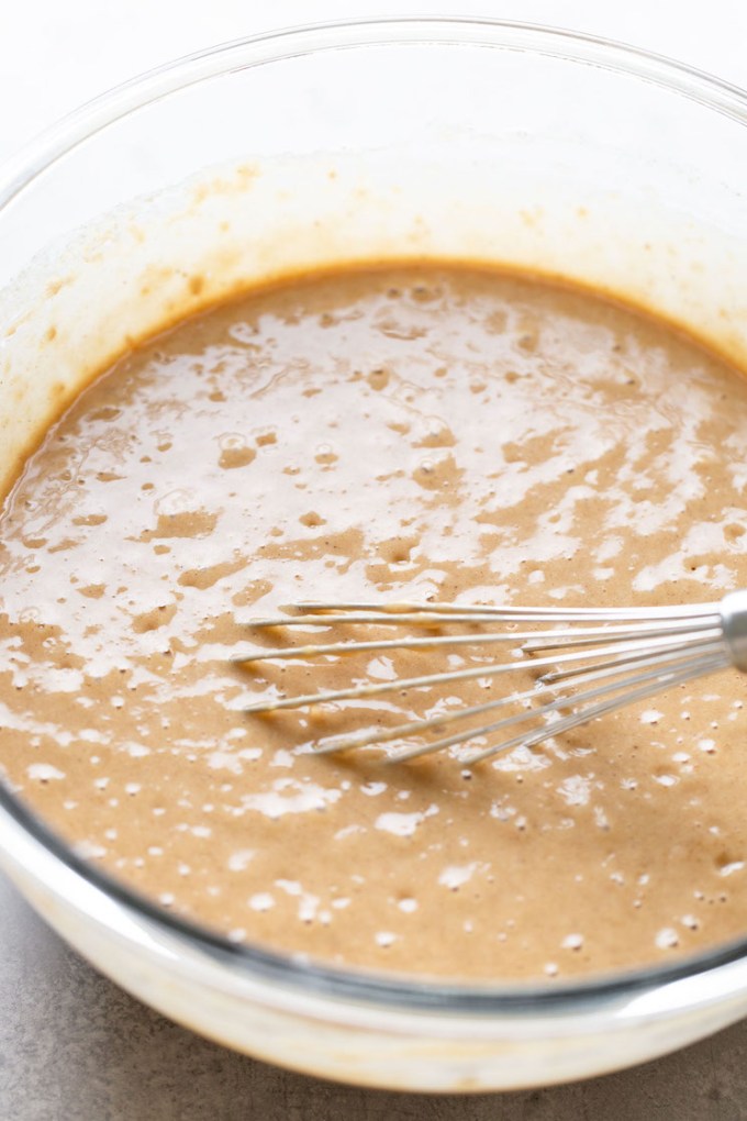 A clear mixing bowl holding the cake batter being mixed with a whisk.