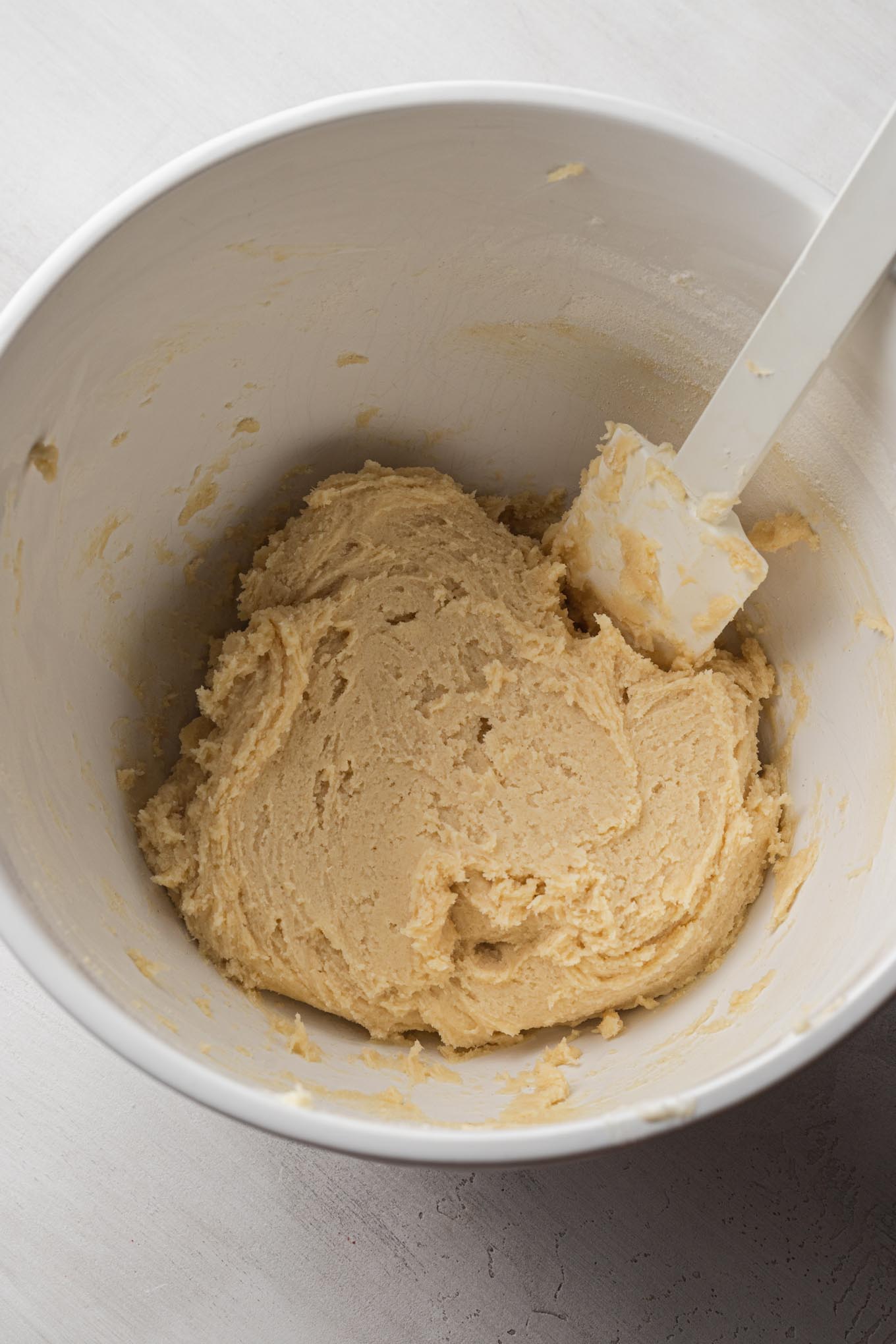 Spritz cookie dough in a white mixing bowl with a rubber spatula.