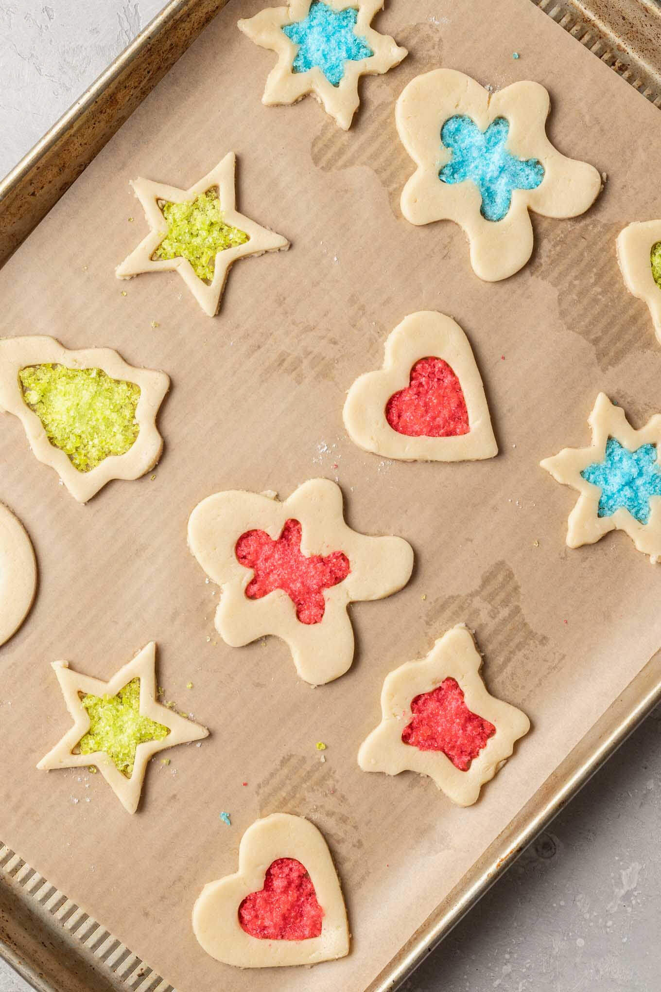 An overhead view of unbaked stained glass cookies on a baking sheet. 