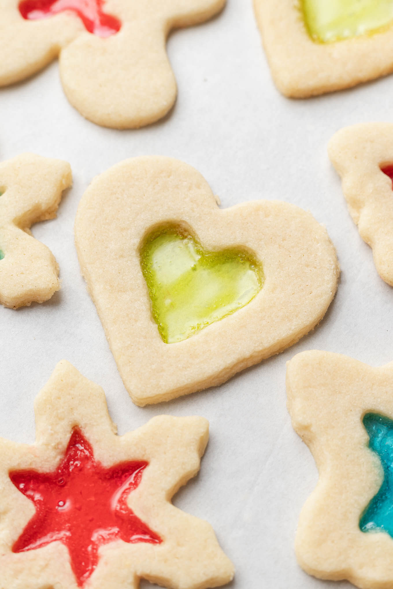 An close-up, overhead view of stained glass window cookies on parchment paper. 