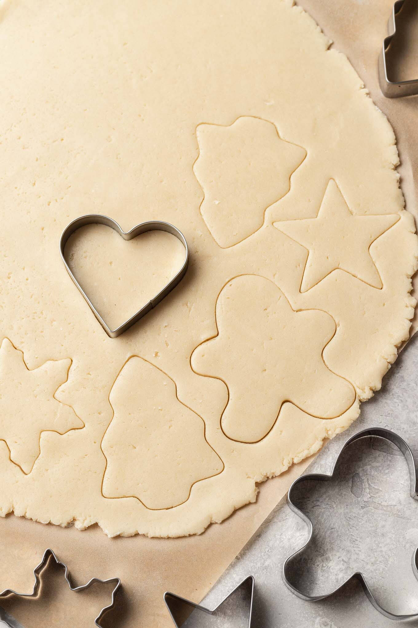 An overhead view of sugar cookie dough being cut into festive shapes. 