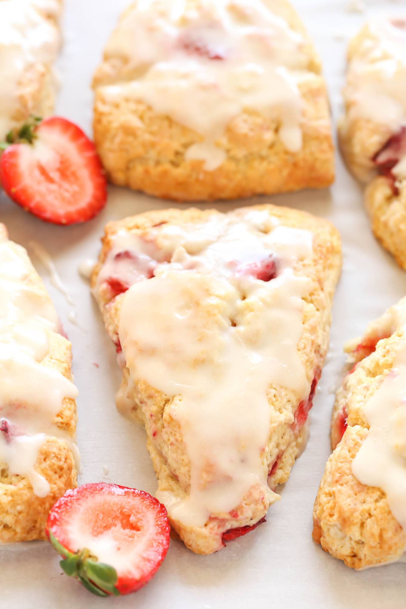 Six strawberry scones topped with glaze. Two strawberry halves rest between the scones. 