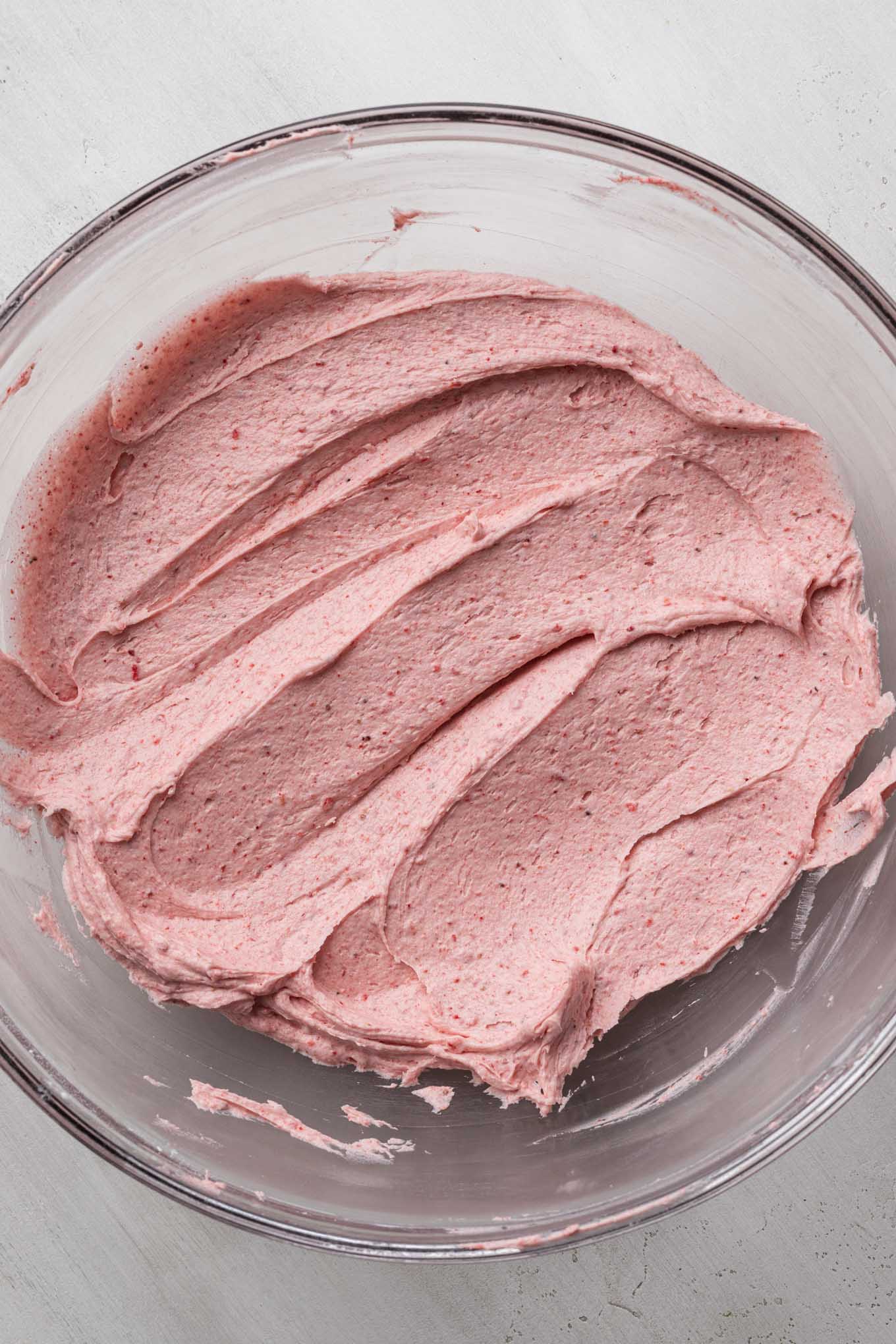 Strawberry frosting mixed together in a glass mixing bowl.