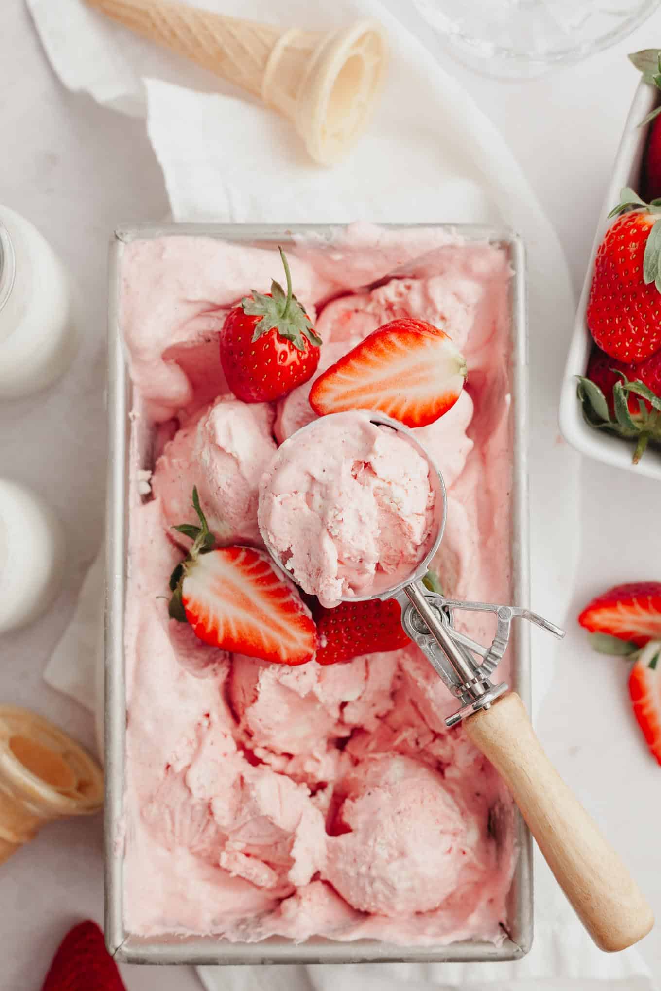 An overhead view of strawberry ice cream garnished with fresh berries in a metal loaf pan.