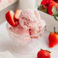 A small glass bowl filled with strawberry ice cream and fresh strawberries.