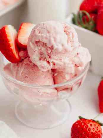 A small glass bowl filled with strawberry ice cream and fresh strawberries.