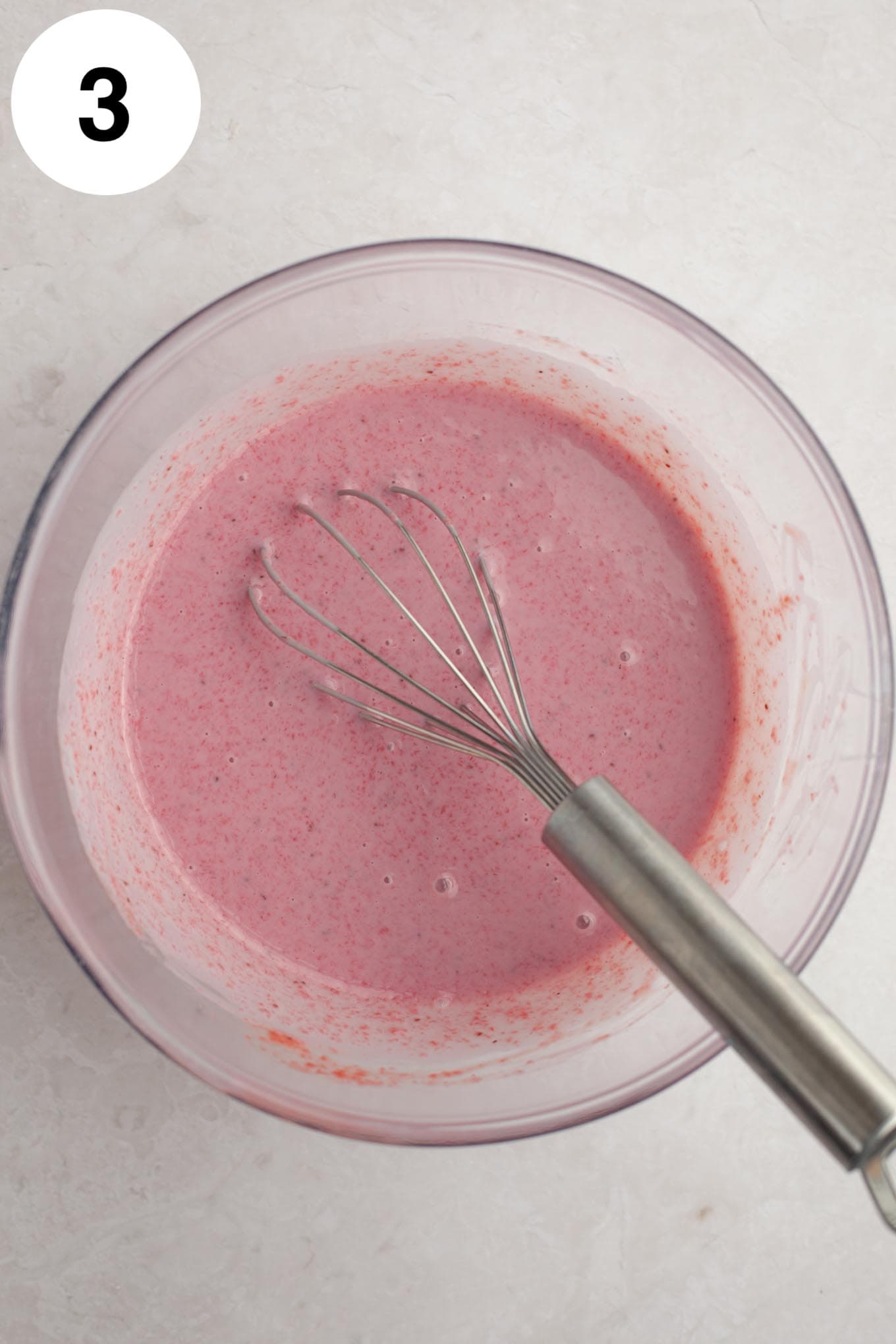 An overhead view of sweetened condensed milk and the strawberry mixture in a glass mixing bowl.