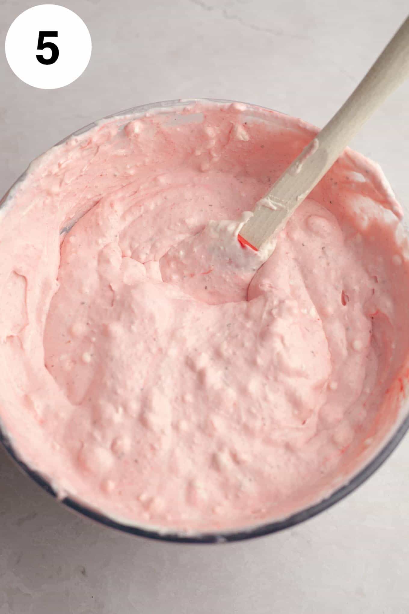 An overhead view of strawberry ice cream in a mixing bowl. 