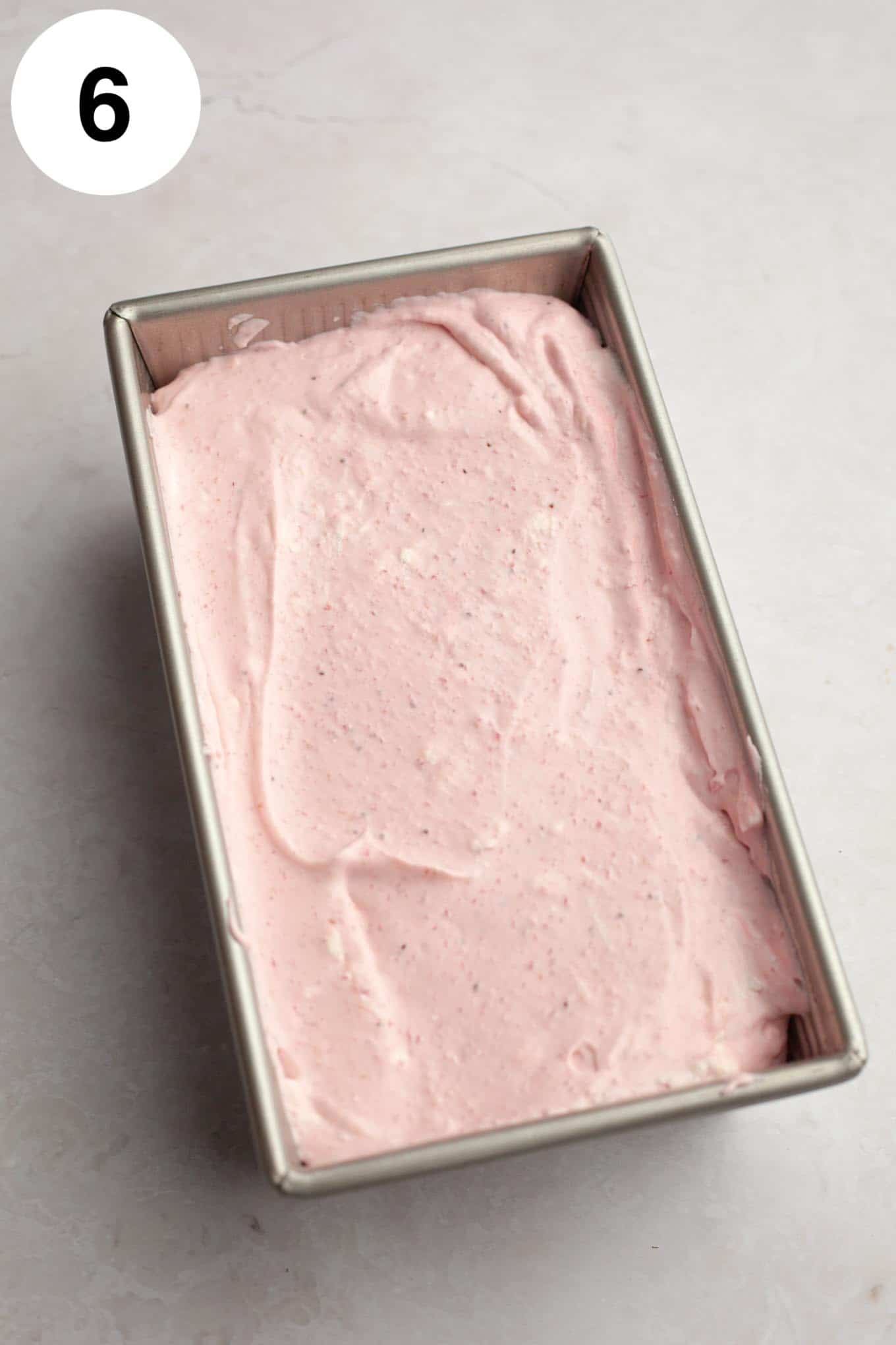 An overhead view of strawberry ice cream in a metal loaf pan. 