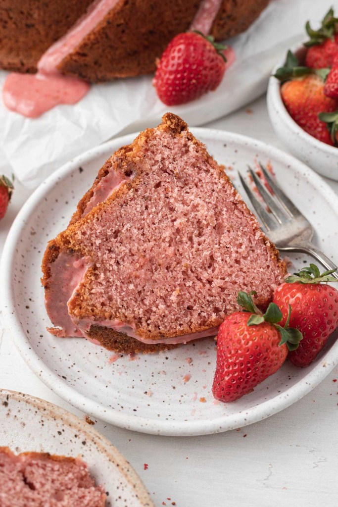 A slice of strawberry glazed pound cake on a white dessert plate with fresh berries and a fork. 