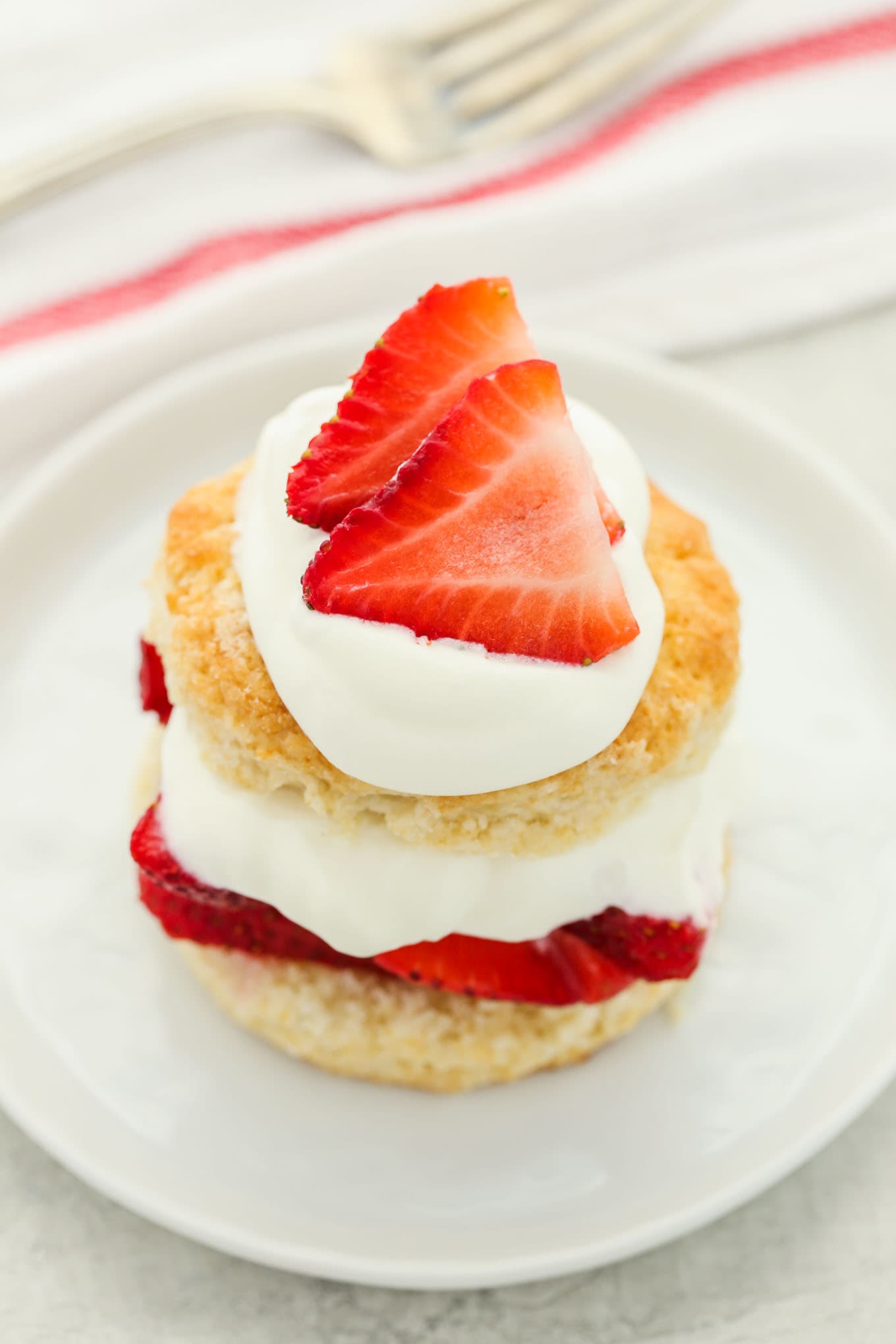 Strawberry shortcake topped with extra whipped cream and sliced strawberries on a white plate.