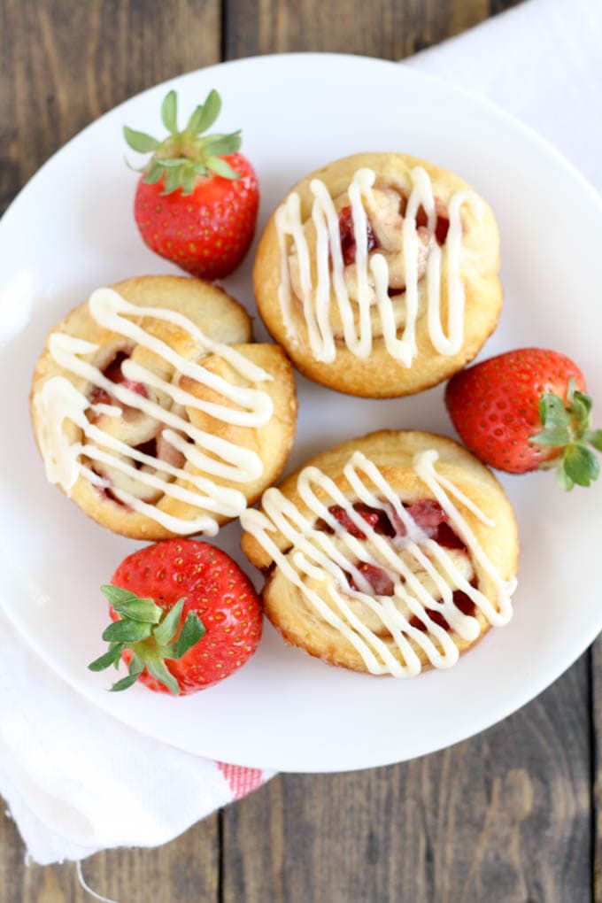 Overhead view of three strawberry rolls and three fresh strawberries on a white plate. 