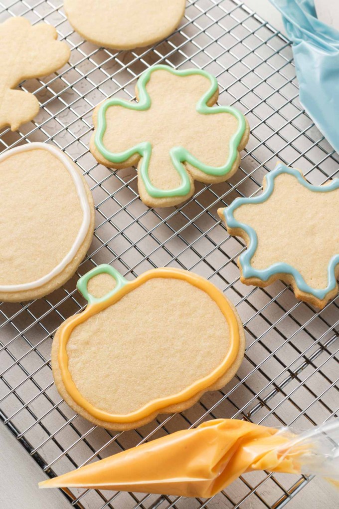 Cut out sugar cookies on a wire cooling rack, outlined with icing.