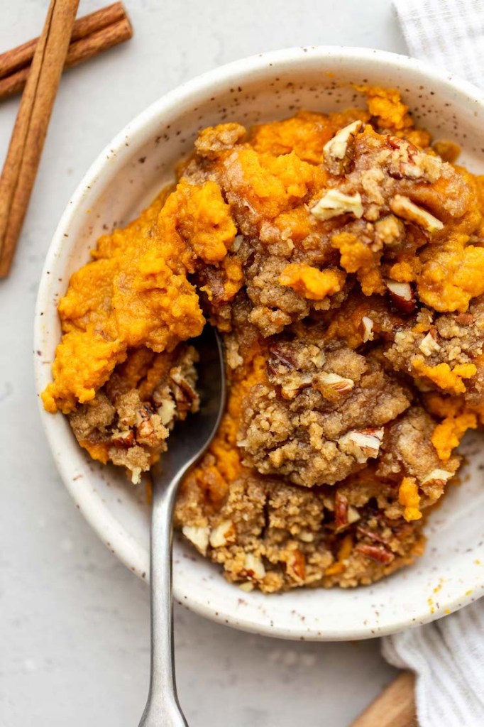 An individual serving of sweet potato casserole in a white speckled bowl.